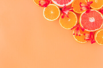 Composition made of slices of citrus fruits (orange, grapefruit) with red flowers  in an orange background