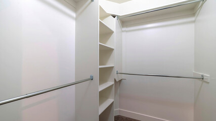 Panorama Hanging metal rods and storage shelves inside empty walk in closet of a new home