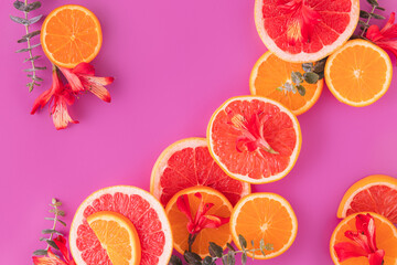 Flat lay made of slices of citrus fruits (orange, grapefruit) with red flowers  in a purple background