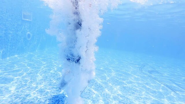 Funny child swim, dive in pool - jump deep down underwater from poolside, slow motion.