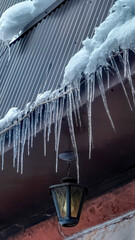 Vertical frame Spiked icicles at the edge of pitched gray roof with clumps of snow in winter