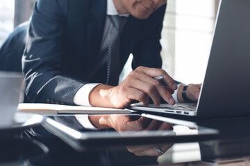 Obraz premium Asian businessman surfing internet working on laptop computer in modern office