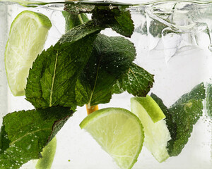 Close up view of the cold and fresh lemonade with lime slices, ice cubes and mint leaves. Texture...