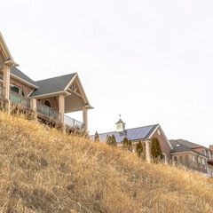Obraz premium Square Beautiful houses sitting on top of grassy slope beneath sky filled with clouds