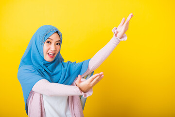 Asian Muslim Arab, Portrait of happy beautiful young woman Islam religious wear veil hijab funny smile she open arms for hug or raise hand to pick up items receive something from above isolated yellow