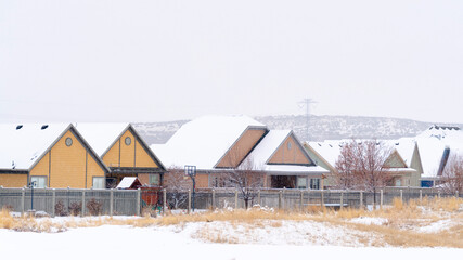 Fototapeta na wymiar Panorama Homes with snowy pitched roofs against hill and cloudy sky on a cold winter day