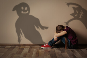 Scared little girl suffering from sciophobia and phantoms behind her. Irrational fear of shadows