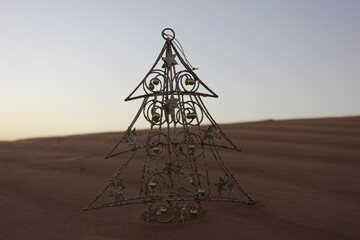 Shiny Christmas tree in desert sand dune. Merry Christmas/Christmas/Happy Holidays/Season's Greetings/Happy New Year/festive/desert/sand dune/celebration concept/background/theme.