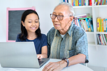 Old man using laptop with his grandchild in library