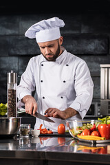 Chef with knife at restaurant kitchen. Male professional cutting tomato.