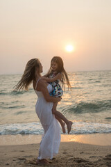 Fototapeta na wymiar Smiling mother and beautiful daughter having fun on the beach at sunset. Mother and daughter on the beach. Very emotional photo