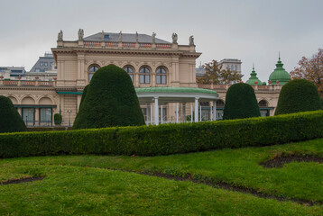 Fototapeta premium Beautiful city park with green lawn in Vienna, Austria. A building with sculptures on the roof in the background.