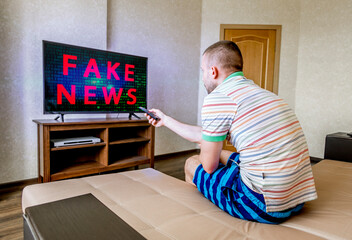 Fototapeta na wymiar man is sitting on a sofa and watching TV with fake news on the screen
