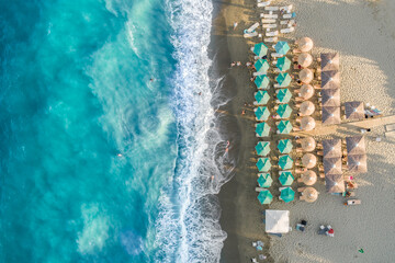 Aerial top down view of a beautiful sandy beach with sunbeds and umbrellas by turquoise wavy sea