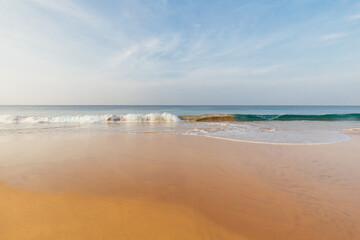 Fototapeta na wymiar Foamy waves on sandy ocean beach under a beautiful sunset sky with clouds on Sri Lanka island.