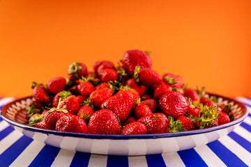 Delicious fresh red strawberries on a large platter on a blue and white striped table.