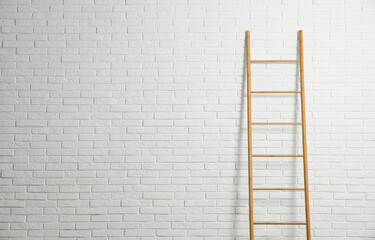 Modern wooden ladder near white brick wall. Space for text