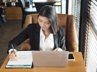 Business woman hand writing on application form with a pencil in the office.Woman in suit sitting with notebook computer.