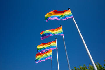 4 rainbow flags as a symbol for homosexuality hang next to each other and the sky is blue