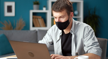 Man wearing protective face mask working on laptop computer staying home during virus outbreak