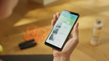 Close-up POV: Fit Woman Holds Smartphone, Uses Fitness Tracking App with Premium Workout Videos, Chooses Desired Exercise Clip. Mock-up Training Application Software