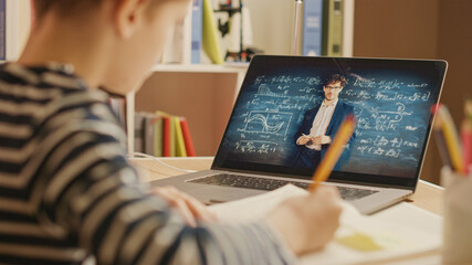 Smart Little Boy Uses Laptop for Video Call with His Teacher. Screen Shows Online Lecture with Teacher Explaining Subject from a Classroom, Boy writes Down Information. E-Education Distance Learning