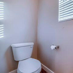 Square frame Toilet at the corner of a bathroom against gray wall with tissue roll holder