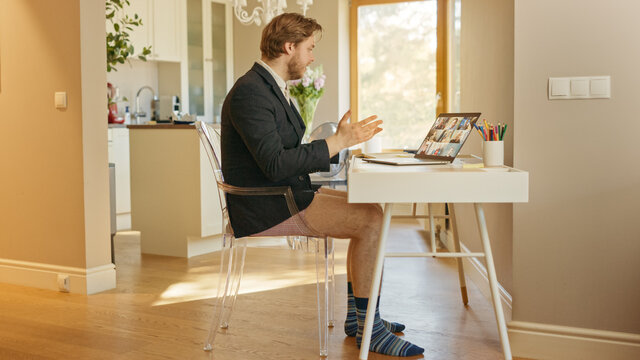 Funny Shot: Businessman Wearing Jacket and No Pants Uses Laptop and Conference Video Call Software App for Board of Directors Online Meeting. Remote Work, Work at Home, Home Office Concept. Side View