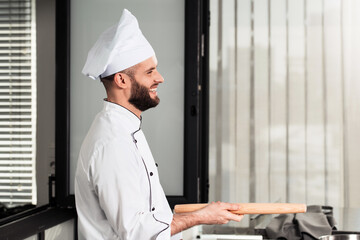 Chef man cooks at the restaurant. Happy professional cook take rolling pin.