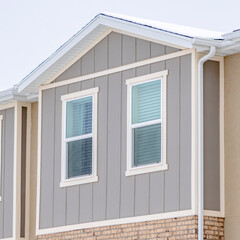 Square crop Snowy roof brick wall and vertical siding at exterior of townhome against sky