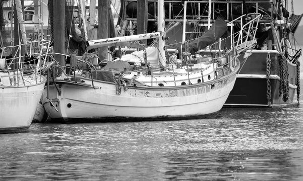A black and white photo of an old sailboat, and shrimp trawler in a creek.