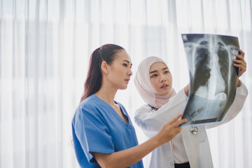 Young Asian woman Muslim doctor  giving advice discussion to patient standing near big window looking chest x-ray film at hospital which excite felling serious. Medicine and health care safe concept.