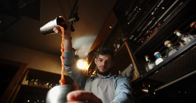 Authentic professional caucasian bartender creating a cocktail drink. Experienced barman pouring alcohol beverage in shaker - food and drink concept close up 4k footage