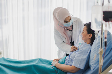 Young Asian woman Muslim doctor giving advice discussion and check up to elderly patient sitting in...