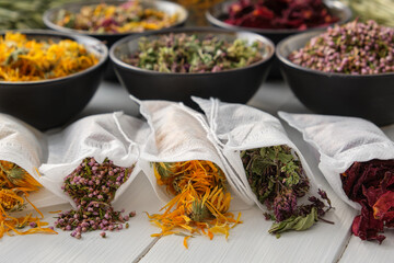 Filter tea bags filled with dry medicinal herbs - marjoram, heather, marigold flowers and rose petals. Bowls of medicinal plants on background. Alternative medicine.