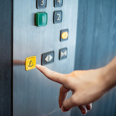 Male forefinger pressing on emergency stop and alarm button in elevator (lift). Mechanical...