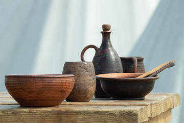 Folk utensil bowls mugs of clay bottles on a wooden table outdoors