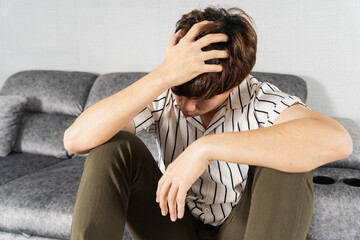 Young man suffering from head pain while sitting on sofa at home. Healthcare medical or daily life concept.
