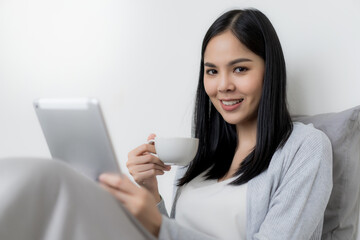 Young beautiful woman checking social media with tablet computer at the the bedroom, living room. Communication and technology concept.