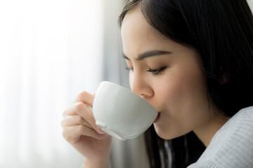 Close up young beautiful woman enjoy drinking with cup of coffee or tea near the window.
