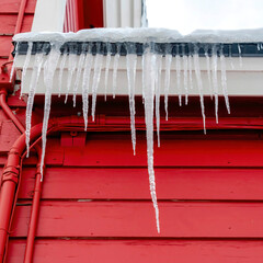 Square Spiked frozen icicles at the roof of home with vibrant red wooden exterior wall