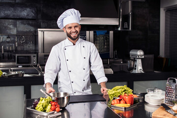 Chef man with raw vegetables at kitchen. Happy professional prepare fresh food.