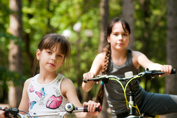 Obraz premium Girls with bicycles. The girls of ten and seven years old with bicycles looks at the camera. Summer time. Outdoor