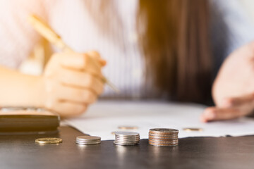 Closeup coins on the desk with businesswoman working on desk office holding pen and using a calculator to calculate the numbers. Expenses, taxes, home budget finance accounting concept.