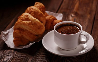 Cup of freshly coffee and tasty croissant on dark wooden table. Sweet and tasty breakfast.
