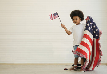 African American boy holding little usa flags standing with us blanket on his shoulder, celebrating...