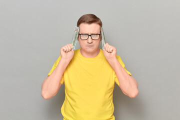 Mature man with glasses is covering his ears with money