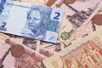 A blue two reais bank note from Brazil close up in macro with a background of brown Egyptian one pound bills