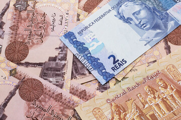 A blue two reais bank note from Brazil close up in macro with a background of brown Egyptian one pound bills