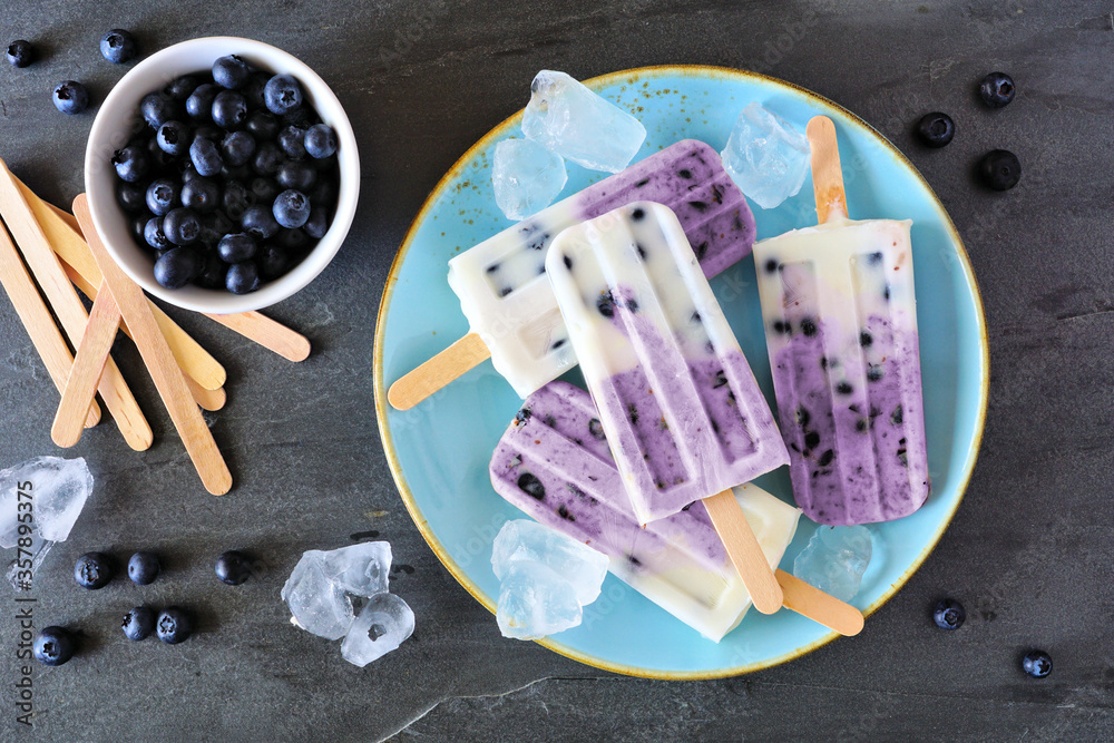 Poster blueberry vanilla yogurt ice pops. top view table scene with over a dark slate background.